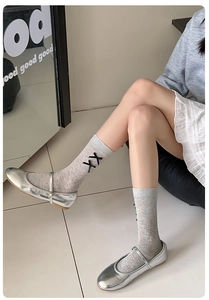 Detail of light gray mid-calf cotton socks featuring black bow ties and silver shoes