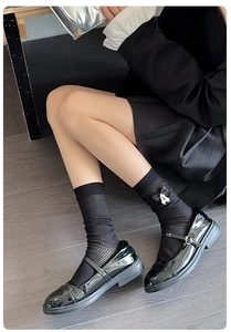 Detail view of black knee-high cotton socks with silk bow and pearl accent in Mary Jane shoes