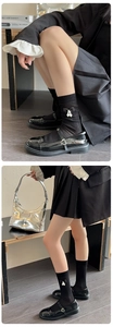 Detail of black cotton mid-calf socks with bow accents and pearl charms worn with Mary Janes