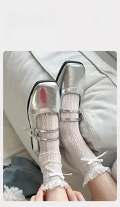 Detail of white lace mesh socks with bow knot paired with silver Mary Jane shoes
