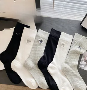 Detail of white and black cotton crew socks with bow and bee embroidery on wood surface