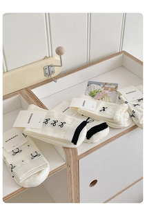 Detailansicht cremeweißer Baumwollsocken mit schwarzer Schleifenstickerei und Rüschenrand