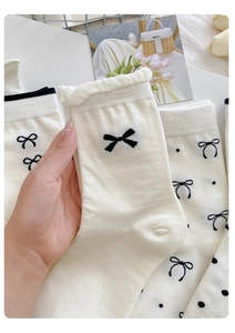 Detailansicht der cremeweißen Baumwollsocken mit schwarzem Schleifenmuster und Rüschen