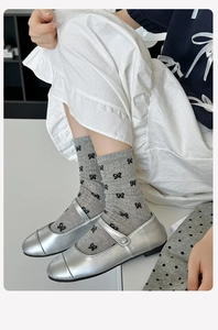 Detail of grey crew socks with black bow patterns paired with silver Mary Jane shoes