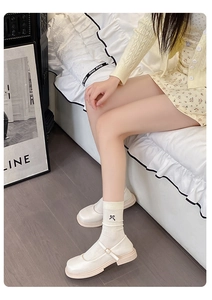 Detail of cream Mary Janes with beige socks featuring a delicate black bow embroidery