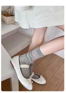 Detail of white slouch socks featuring pink bow embroidery and fine ribbed knit texture