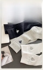 Close-up of cotton ribbed socks in white, black and grey with small bee embroidery