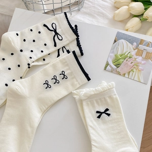Drei Paar cremefarbene Baumwollsocken mit schwarzen Schleifen in minimalistischem Design