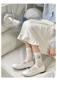 Detail of white rib-knit mid-calf socks with black bow embroidery and satin Mary Jane shoes
