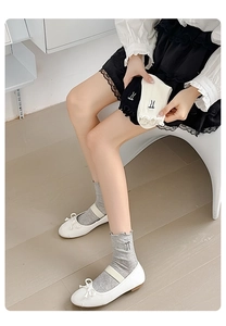 Detail of sweet ruffle cuffs and minimal embroidery on grey, black, and white socks