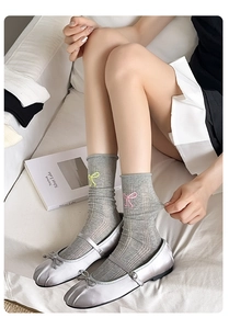 Détail de chaussettes mi-hautes grises côtelées avec broderie nœud rose et jaune