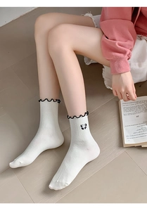Close-up of white crew socks with black ruffled edges and cute bow details on feet