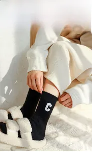 Detail of embroidered letter C on black wool socks paired with plush slippers
