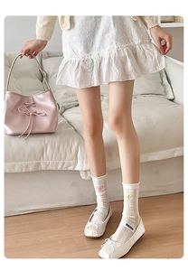 Détail de chaussettes en maille crème avec broderie nœud rose et ballerines blanches
