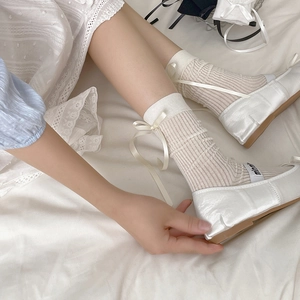 White satin ballet flats with ribbon socks featuring vertical stripes in a soft setting