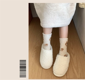 Detail of white plush slippers and beige socks with brown cartoon bear patterns
