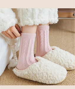 Detail of pink cable knit socks and white plush slippers on a woven rug backdrop