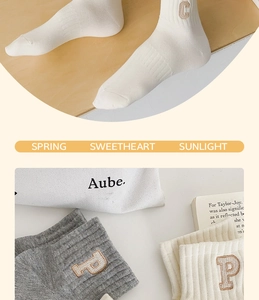 Close-up of ribbed cotton crew socks with minimalist letter embroidery in neutral colors