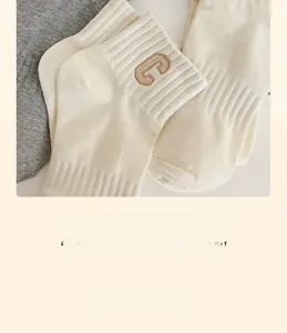 Detailed macro view of beige cotton socks featuring brown embroidered letter C on ribbed cuff