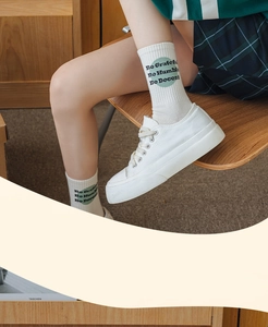 Close-up of white cotton mid-calf socks with Be Grateful green graphic and rib knit cuffs