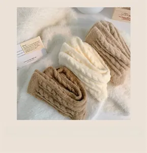 Detail of three cable-knit infinity scarves in brown, cream, and tan on a soft white rug