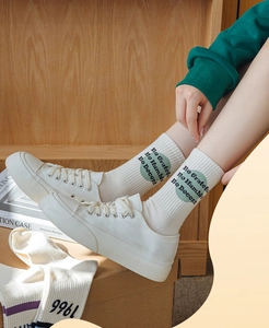 Detail of white cotton crew socks with green circular graphic and typography on ribbed fabric