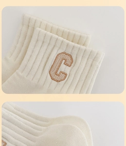 Detail view of cream white ribbed socks with brown embroidered letter C on the side