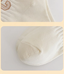 Detailed close-up of cream knit socks featuring a brown embroidered letter G and toe seam
