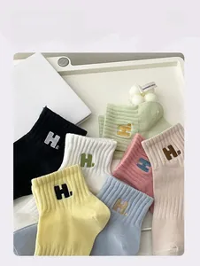 Detail of candy-colored cotton socks with H-letter embroidery on a white decorative tray