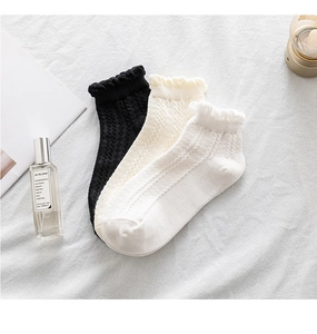 Detailed knit texture of three pairs of women's frilly socks in black, beige and white
