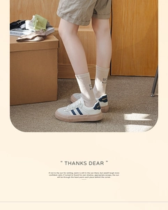 Close-up of white rib-knit socks with embroidery and blue striped sneakers in a warm room