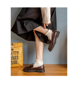 Detail of white lace frill socks paired with vintage brown bow platform loafers on wood floor