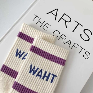 Off-white cotton crew socks with purple stripes and WAHT embroidery in a flat lay view