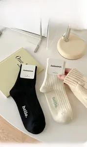 Detail of ribbed knit combed cotton crew socks with hello text embroidery in cream and black