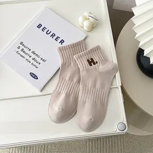 Minimalist beige cotton socks with brown H embroidery and ribbed cuffs on white tray