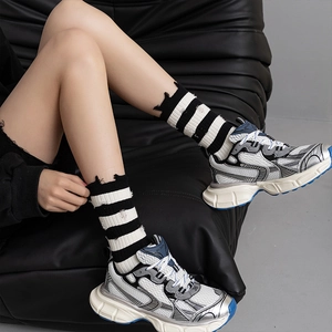 Women's distressed black and white striped crew socks paired with chunky silver sneakers