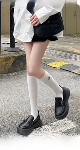 Detailed side view of white knee-high socks with black cross embroidery and platform loafers