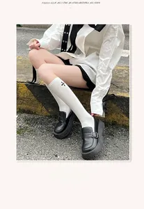 Detail of white calf socks with black cross embroidery and platform loafers