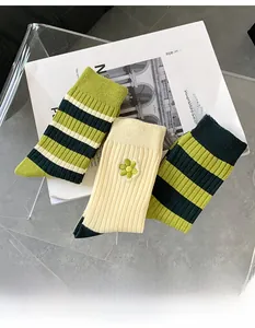 Detailansicht von drei grünen Baumwollsocken mit Streifen und Blumenstickerei-Details