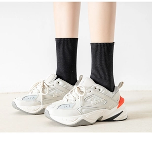 Close-up of white leather daddy sneakers with orange details and black ribbed socks