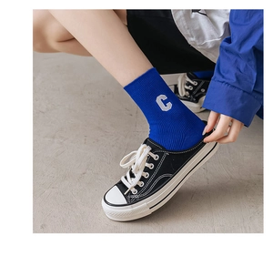 Details von kleinblauen Baumwoll-Rippsocken mit weißer C-Stickerei und Segeltuchschuhen