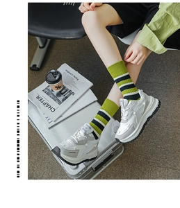 Detail von grün-schwarz gestreiften Socken mit Mesh-Sneakern auf silbernem Reisekoffer