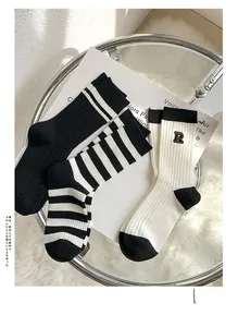 Detail of three black and white cotton socks with R embroidery on white magazine
