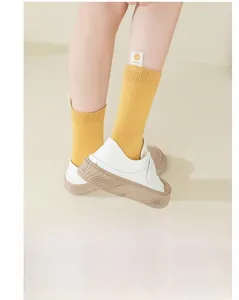 Detail of yellow ribbed socks with smiley face tag worn with white canvas platform shoes