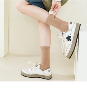 Detailed close-up of khaki knitted socks with a smile face tag and white star sneakers
