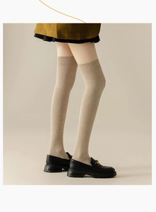 Detailed knit texture of oat-colored over-the-knee socks with ribbed cuffs
