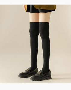 Close-up of black ribbed over-the-knee socks paired with golden horsebit loafers