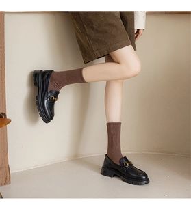Dettaglio mocassini neri platform con fibbia dorata e calze marroni in maglia