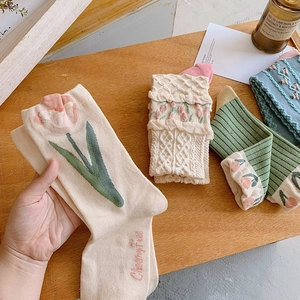 Chaussettes en tricot pastel avec broderie tulipe et dentelle sur fond de bois