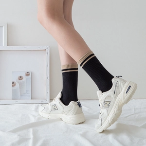 Beige mesh sneakers styled with black striped crew socks on a minimalist background